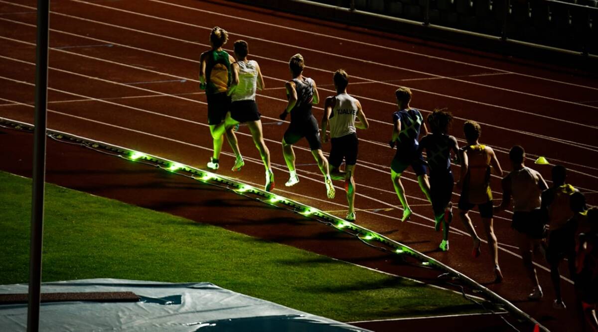 Distance runners following a line of green WaveLight pacing LEDs along a track curb